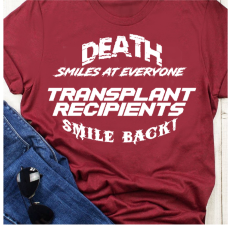 “Death smiles—transplant recipients smile back tee, red shirt with white  vinyl text, flat lay”