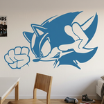 A large blue Sonic the Hedgehog wall decal is displayed on a white bedroom wall above a wooden desk and chair, with a bed and other room decor visible.