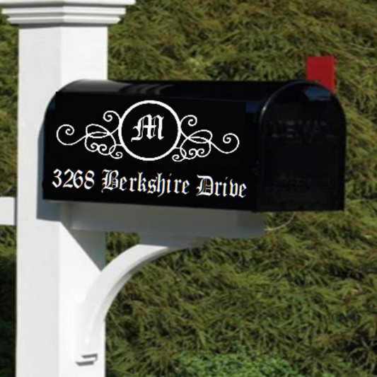 Black mailbox with decorative monogram and address on a white post against a green bush background