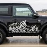 A black Ford Bronco parked outdoors on a concrete surface, shown in side profile. The vehicle features a large white graphic decal on the side depicting a mountain range with a sasquatch/bigfoot figure.