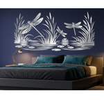 A modern bedroom scene featuring a large, decorative white wall mural of water lilies, dragonflies, and reeds above a low-profile platform bed with dark bedding and teal pillows, set against a dark navy blue wall.
