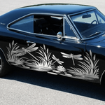 A black classic muscle car with white dragonfly and reeds printed along the side, parked on a gray asphalt surface.