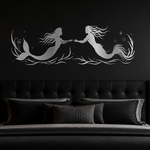 A black bed in a dark, moody bedroom with a large silver mermaid and merman wall art piece on the wall above the headboard.