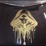 A gold vinyl decal of a hooded grim reaper with dripping paint effects, applied to the glossy black hood of a car.